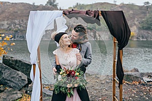 Groom tenderly embracing her beautiful bride by behind. Autumn wedding ceremony in rustic style outdoors. Happy
