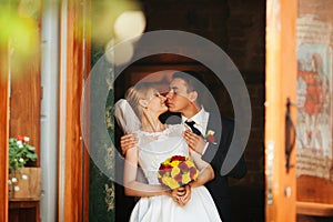 Groom touches bride's nose tenderly holding her from behind in a