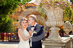 Groom touching bride near carousel in park