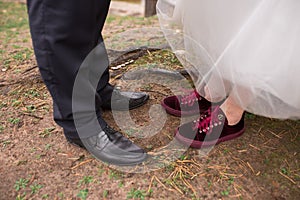 The groom in trousers and black shoes and the bride in red sneakers showing their wedding shoes.