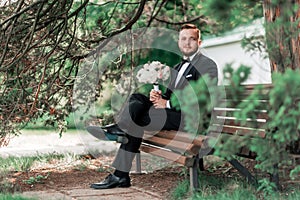 Groom is waiting for the bride sitting sitting on the bench.