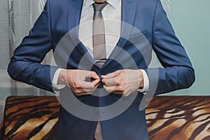 Groom is wearing the blue wedding suit. Stylish man is holding his tie in hands. Celebration day ceremony. Wedding fashion details