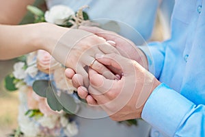 Groom wears bride a wedding ring Bride hand holds a beautiful wedding bouquet.