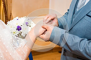 Groom wears bride a wedding ring Bride hand holds a beautiful wedding bouquet