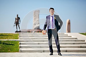 Groom with wedding bouquet on background of monument to soldiers.