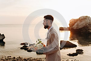 Groom with a wedding bouquet on the beach. Groom in boho style.