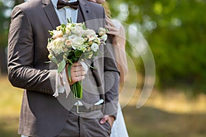 The groom in a wedding suit holds a beautiful wedding bouquet of roses in a pink shade