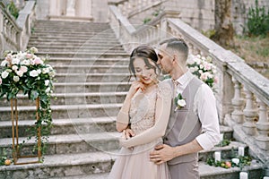 Groom whispers in the bride ear while embracing her on the stone steps of an ancient villa