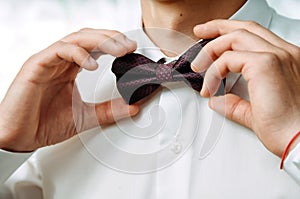 The groom in a white collar fixing his bow tie
