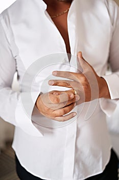 Groom in a white unbuttoned shirt adjusts the ring on his finger. Cropped. Faceless