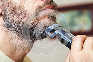 Grooming beard with gray hair trimmer closeup