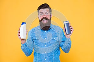 Grooming at every opportunity. Bearded man hold shampoo bottles yellow background. Cosmetics and toiletries. Hygiene and