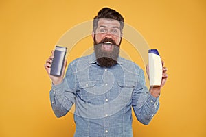 Grooming at every opportunity. Bearded man hold shampoo bottles yellow background. Cosmetics and toiletries. Hygiene and