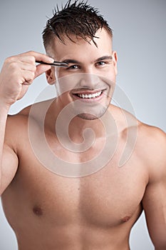 Grooming to perfection. Portrait of a young handsome man tweezing his eyebrows against a grey background.