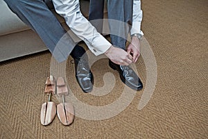 A groomsman ties up his new shoes beside a pair of shoe stretchers
