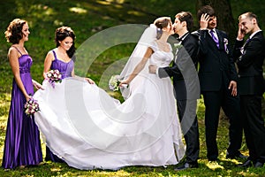 Groomsmen look funny standing behind a kissing wedding couple