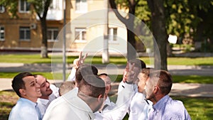 Groomsmen toss groom in the air. Man flexing and having fun with best friends on wedding day in park. Cheerful guys