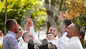 Groomsmen toss groom in the air. Man flexing and having fun with best friends on wedding day in park. Cheerful guys