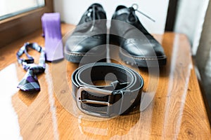 Groomâ€™s accessories: black leather belt in focus, black shoes, necktie.