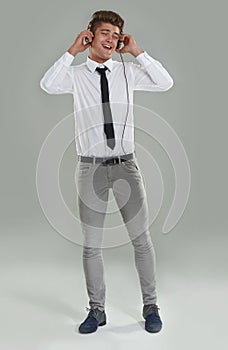 Grooving through the work week. A young man in a shirt and tie dancing while listening to music on his headphones.