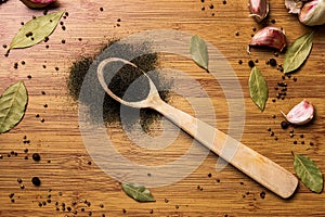 Ground black pepper with a wooden inscription `Pepper` on a wooden background. View from above. Garlic and bay leaf on the backg