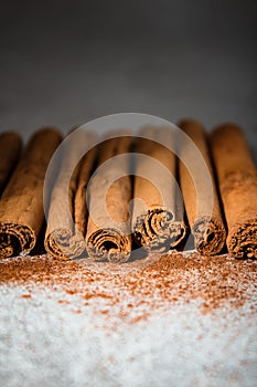 Ground Ceylon cinnamon sprinkled in front of real cinnamon sticks on a light background