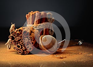 Ground cinnamon, cinnamon sticks, tied with jute rope on a black reflective background