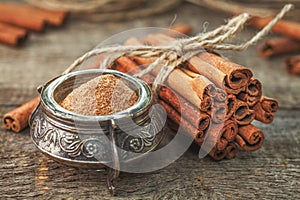 Ground cinnamon, cinnamon sticks, tied with jute rope on old wooden background in rustic style.