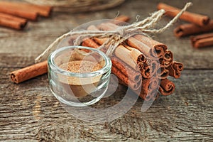 Ground cinnamon, cinnamon sticks, tied with jute rope on old wooden background in rustic style.