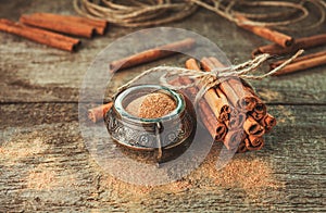 Ground cinnamon, cinnamon sticks, tied with jute rope on old wooden background in rustic style