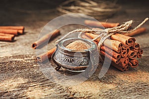 Ground cinnamon, cinnamon sticks, tied with jute rope on old wooden background in rustic style.