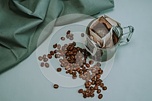 Ground coffee, a bag for coffee drops and a transparent mug on the table. Drop coffee on a gray background with coffee beans.