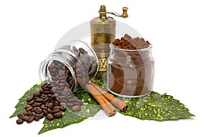 Ground coffee and coffee beans in glassy bowls, cinnamon and coffee grinder on green leaves