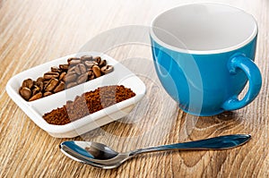 Ground coffee and coffee beans in partitioned bowl, empty coffee cup, spoon on wooden table