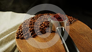 Ground coffee in portafilter on wooden board with coffee beans and dissipating steam. Freshly ground coffee in filter