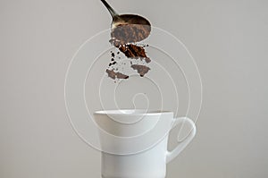 Ground coffee is poured into a white cup with a spoon