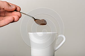 Ground coffee is poured into a white cup with a spoon