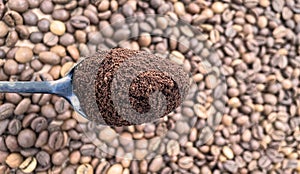 Ground coffee powder in a metal spoon in the foreground, against the background of roasted aromatic coffee beans. Coffee