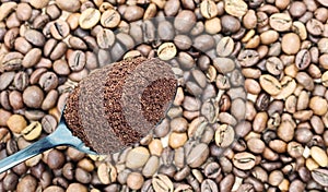 Ground coffee powder in a metal spoon in the foreground, against the background of roasted aromatic coffee beans. Coffee