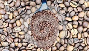 Ground coffee powder in a metal spoon in the foreground, against the background of roasted aromatic coffee beans. Coffee