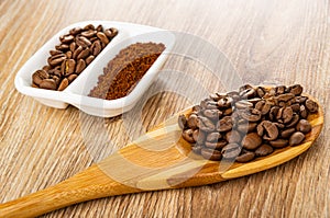 Ground coffee and roasted coffee beans in partitioned bowl, coffee beans in spoon on wooden table
