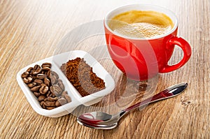 Ground coffee and roasted coffee beans in partitioned bowl, cup with espresso, spoon on table