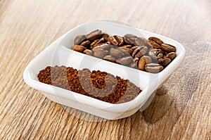 Ground coffee and roasted coffee beans in partitioned bowl on wooden table