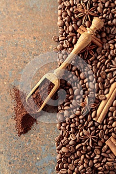 Ground coffee in a spoon and coffee beans with cinnamon and anise on a rusty metal background
