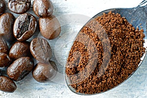 Ground coffee in a spoon and coffee beans on a wooden background