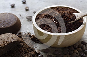 Ground coffee in a wooden bowl on concrete background with a pile of arabica coffee beans