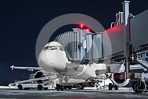 Ground handling of a white passenger aircraft at the boarding bridge on the airport apron at night. Loading baggage on the