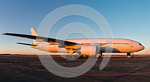 Ground handling of white wide-body passenger airplane at the airport apron in the evening sun