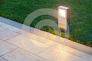 Ground lamp lighting marble walkway in the evening park.