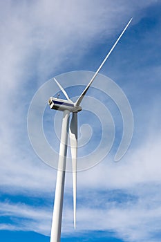 Ground low view on wind propeller turbine, blue sky, and clouds.
